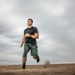 A muscular man running on sandy terrain under cloudy skies, promoting fitness and adventure.